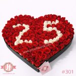 Caja corazón con 130 rosas rojas y números blancos, arreglo floral sofisticado para regalar en ocasiones especiales.